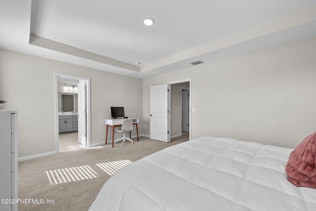 bedroom with light carpet, ensuite bathroom, and a raised ceiling