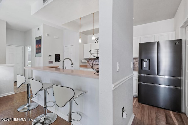 kitchen featuring dark hardwood / wood-style flooring, a breakfast bar, stainless steel fridge with ice dispenser, white cabinetry, and hanging light fixtures