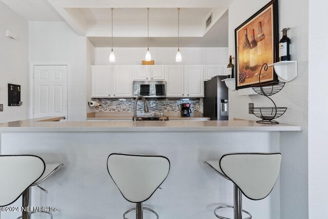 kitchen featuring white cabinetry, stainless steel appliances, backsplash, kitchen peninsula, and pendant lighting