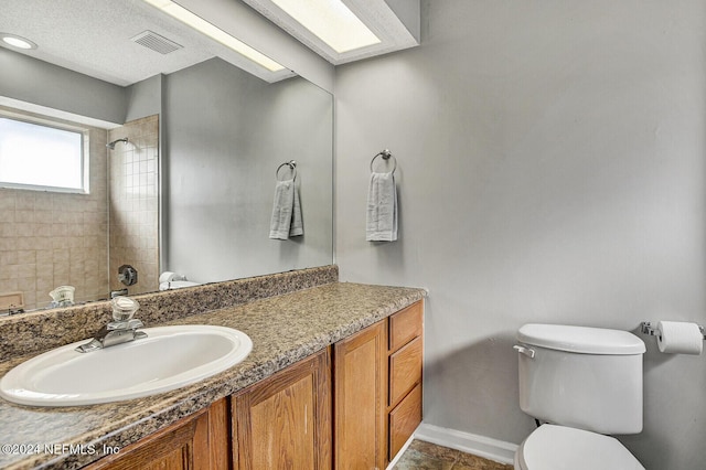 bathroom featuring a tile shower, vanity, and toilet