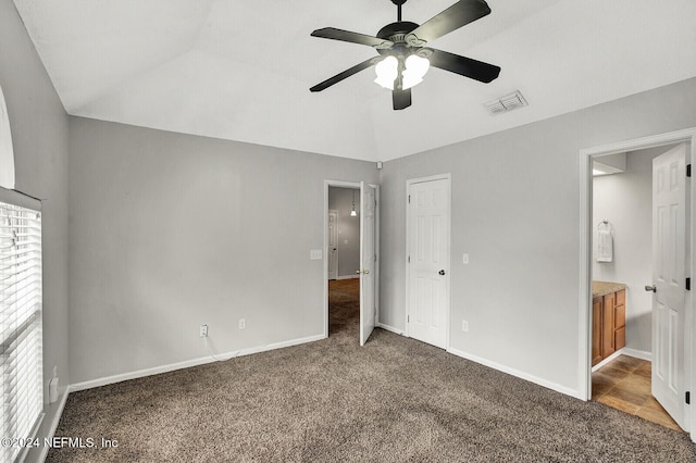 unfurnished bedroom with ensuite bathroom, ceiling fan, dark carpet, and vaulted ceiling