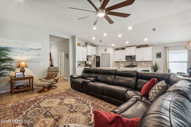 living room with ceiling fan, light wood-type flooring, and vaulted ceiling