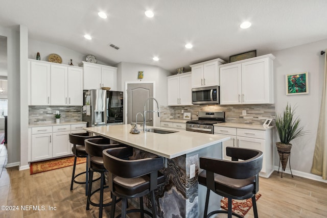 kitchen featuring white cabinets, appliances with stainless steel finishes, light hardwood / wood-style flooring, and vaulted ceiling