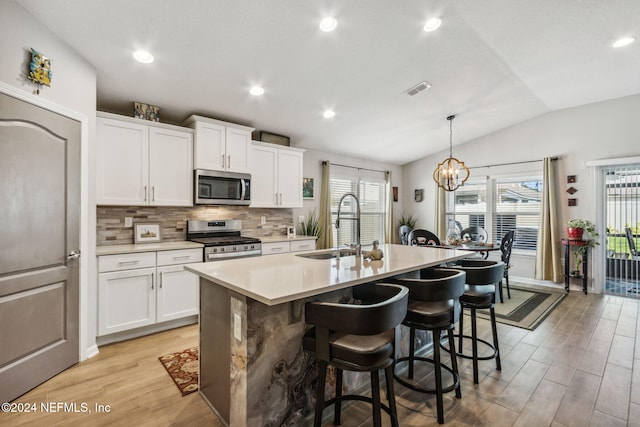 kitchen featuring appliances with stainless steel finishes, light wood-type flooring, a kitchen island with sink, white cabinetry, and lofted ceiling