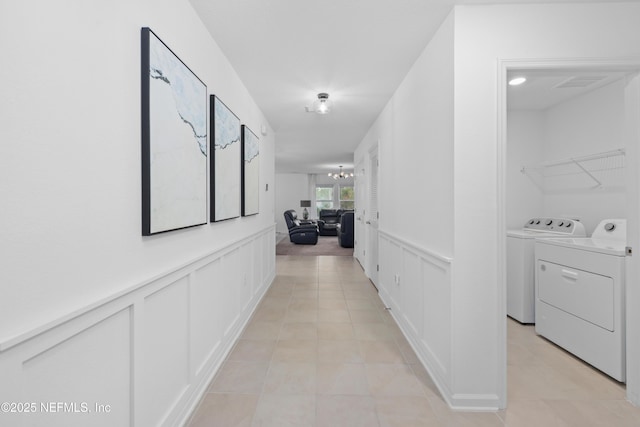 hallway featuring visible vents, a decorative wall, wainscoting, separate washer and dryer, and a chandelier