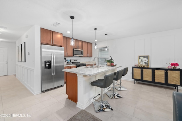 kitchen with a center island with sink, appliances with stainless steel finishes, hanging light fixtures, a kitchen bar, and a sink