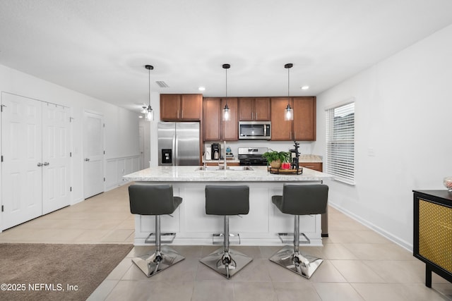 kitchen featuring an island with sink, appliances with stainless steel finishes, a kitchen breakfast bar, decorative light fixtures, and a sink