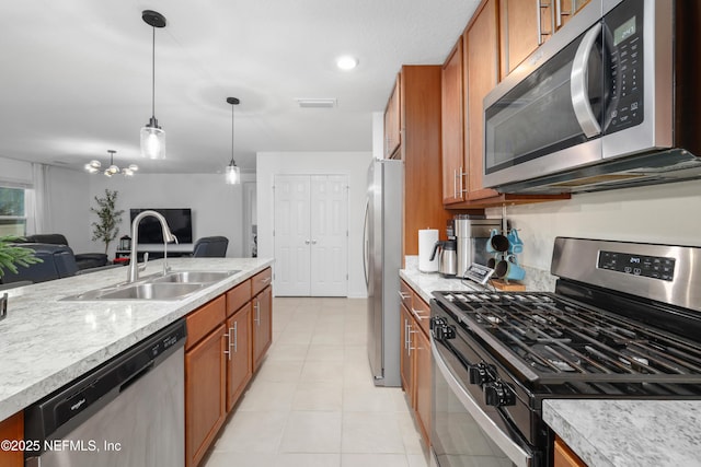 kitchen with pendant lighting, appliances with stainless steel finishes, brown cabinetry, open floor plan, and a sink