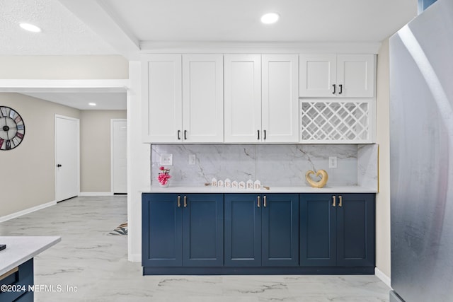 kitchen featuring white cabinets, blue cabinetry, stainless steel refrigerator, and tasteful backsplash