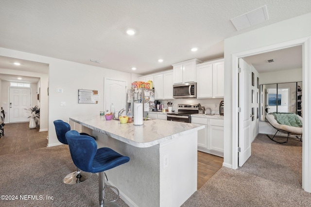 kitchen with hardwood / wood-style floors, white cabinets, an island with sink, appliances with stainless steel finishes, and a kitchen bar