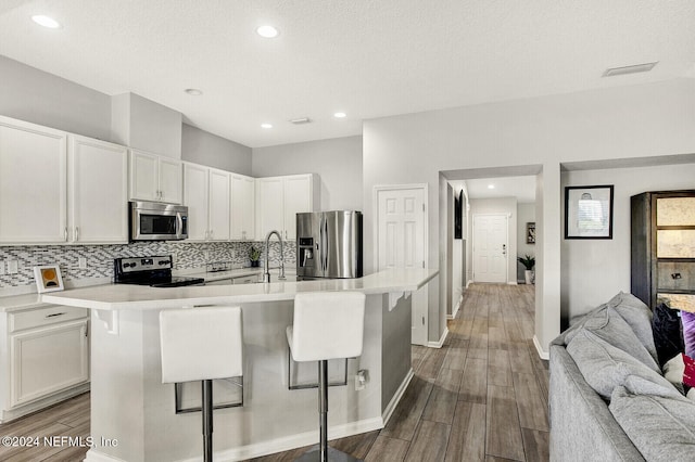 kitchen featuring white cabinets, a kitchen bar, an island with sink, and appliances with stainless steel finishes