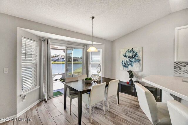 dining space featuring a textured ceiling, a water view, lofted ceiling, and light hardwood / wood-style floors