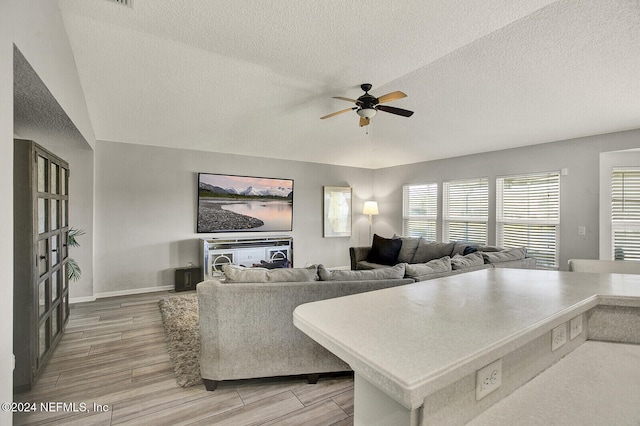 living room featuring a textured ceiling, hardwood / wood-style flooring, vaulted ceiling, and ceiling fan