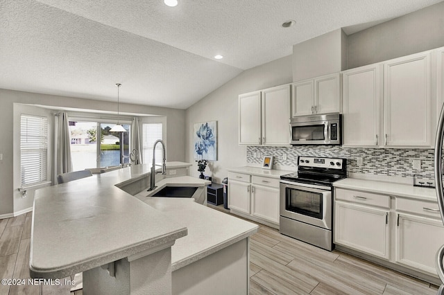 kitchen featuring appliances with stainless steel finishes, a kitchen island with sink, pendant lighting, a breakfast bar area, and lofted ceiling