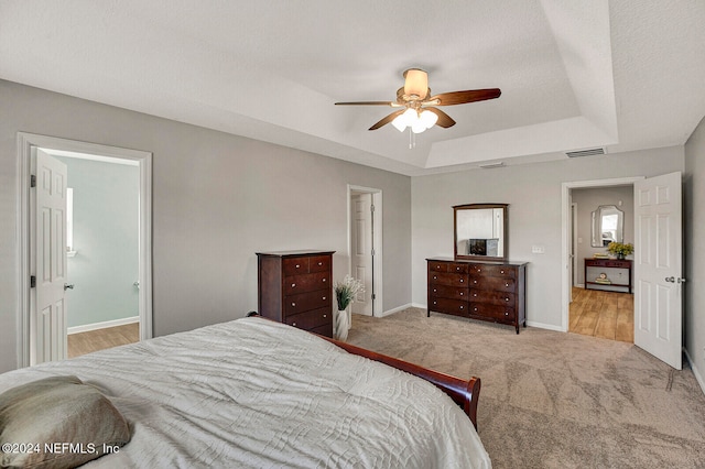 carpeted bedroom featuring a tray ceiling, ensuite bath, ceiling fan, and a textured ceiling