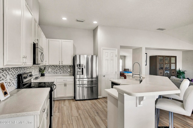 kitchen featuring vaulted ceiling, an island with sink, appliances with stainless steel finishes, a kitchen bar, and white cabinetry