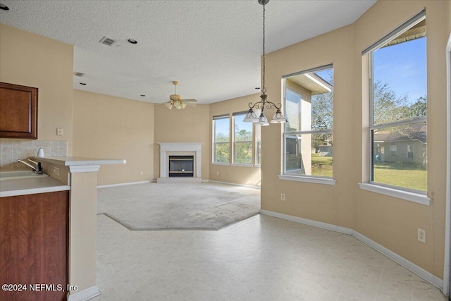 unfurnished living room with ceiling fan, sink, a textured ceiling, and a wealth of natural light