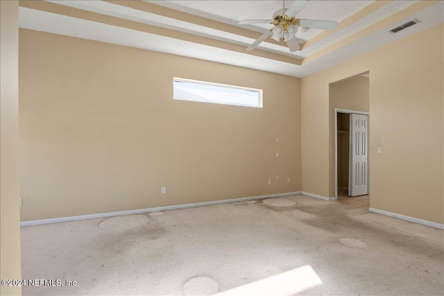 empty room with light carpet, a textured ceiling, a tray ceiling, and ceiling fan