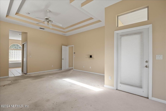 empty room featuring ceiling fan, a raised ceiling, and light carpet