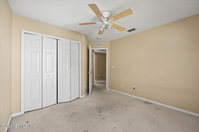 unfurnished bedroom featuring light carpet, a textured ceiling, a closet, and ceiling fan