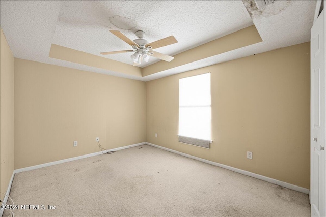 empty room featuring a textured ceiling, light colored carpet, a raised ceiling, and ceiling fan