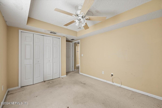 unfurnished bedroom featuring ceiling fan, a raised ceiling, a textured ceiling, light carpet, and a closet