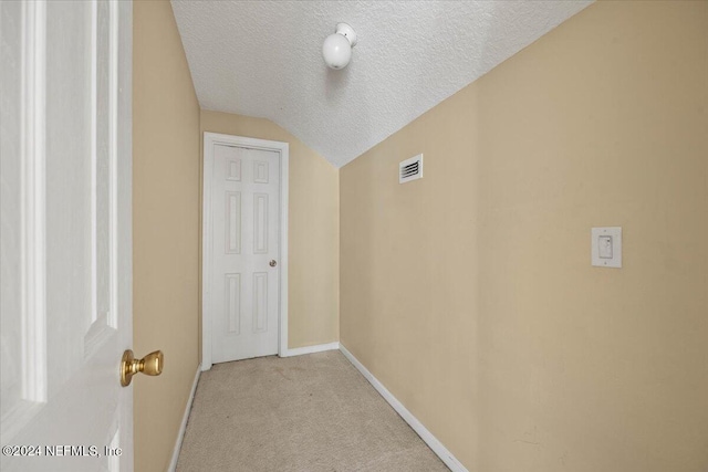 corridor featuring light carpet, a textured ceiling, and vaulted ceiling