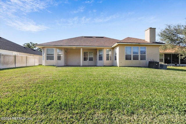 rear view of property with central air condition unit and a lawn