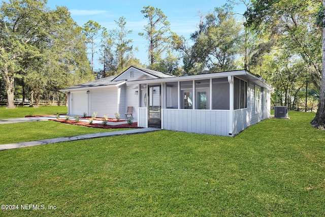 view of front of property with central AC, a sunroom, a front lawn, and a garage