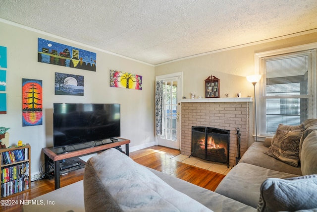 living room with a textured ceiling, light hardwood / wood-style floors, a brick fireplace, and ornamental molding