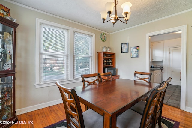 dining space with a textured ceiling, an inviting chandelier, crown molding, and light hardwood / wood-style flooring