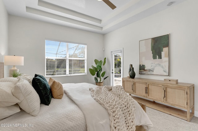 carpeted bedroom with ceiling fan, access to exterior, and a tray ceiling