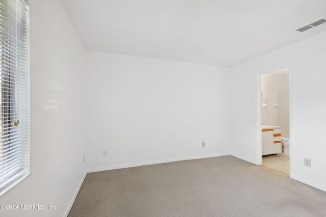 unfurnished bedroom with connected bathroom and light colored carpet