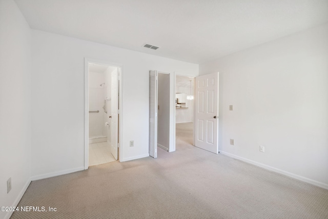 unfurnished bedroom with light carpet, ensuite bath, and a closet