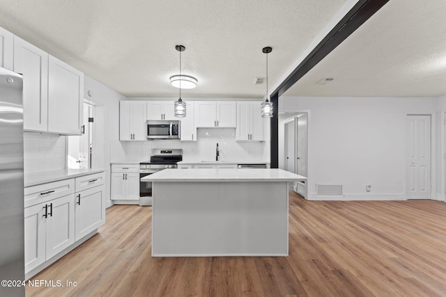 kitchen featuring white cabinetry, stainless steel appliances, decorative light fixtures, and light hardwood / wood-style floors