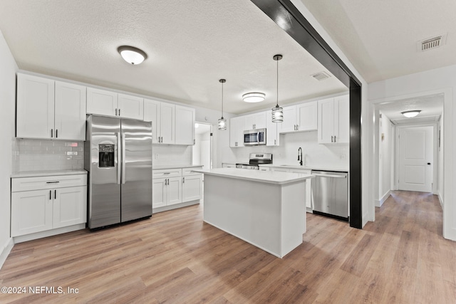 kitchen featuring pendant lighting, white cabinets, appliances with stainless steel finishes, and light hardwood / wood-style flooring