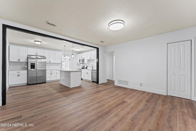 kitchen featuring appliances with stainless steel finishes, white cabinetry, hanging light fixtures, and hardwood / wood-style floors