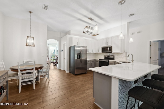 kitchen with white cabinetry, sink, stainless steel appliances, kitchen peninsula, and decorative light fixtures