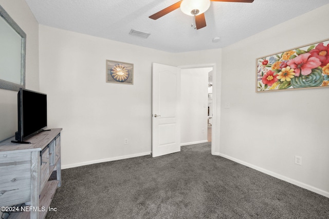 interior space featuring ceiling fan, dark carpet, and a textured ceiling