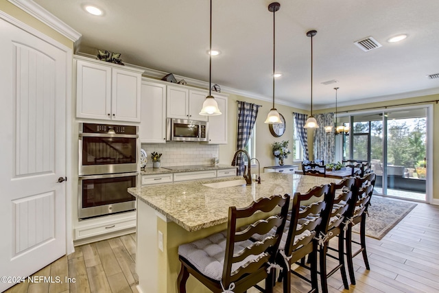 kitchen with decorative light fixtures, a kitchen island with sink, stainless steel appliances, and a breakfast bar area