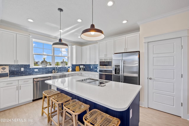 kitchen with a center island, hanging light fixtures, ornamental molding, appliances with stainless steel finishes, and white cabinetry