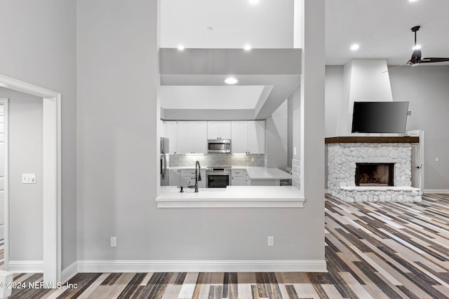 kitchen with white cabinets, a stone fireplace, hardwood / wood-style flooring, decorative backsplash, and stainless steel appliances