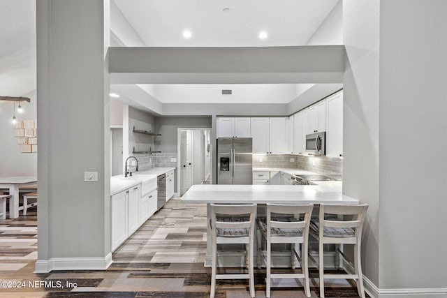 kitchen featuring kitchen peninsula, light hardwood / wood-style flooring, white cabinets, and appliances with stainless steel finishes