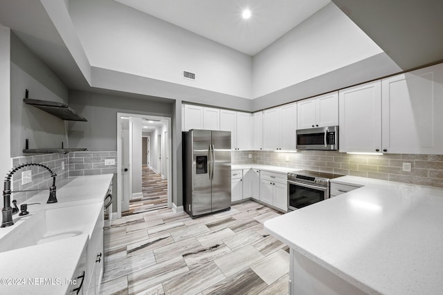 kitchen with sink, a towering ceiling, decorative backsplash, white cabinets, and appliances with stainless steel finishes