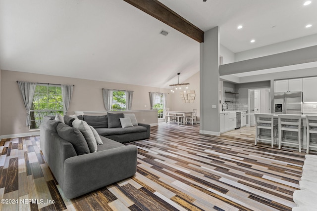 living room with sink, an inviting chandelier, beamed ceiling, high vaulted ceiling, and light wood-type flooring