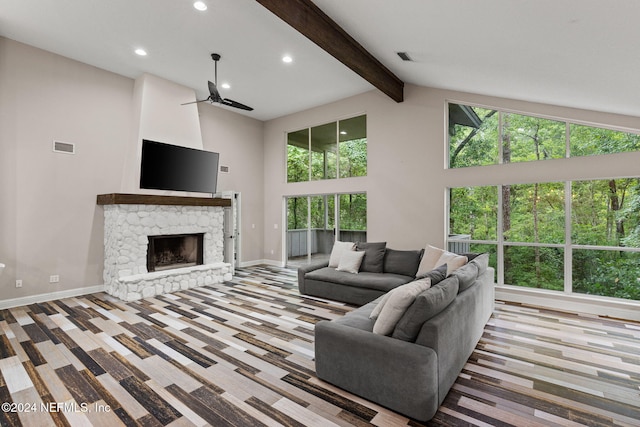 living room with beam ceiling, ceiling fan, a stone fireplace, light hardwood / wood-style flooring, and high vaulted ceiling