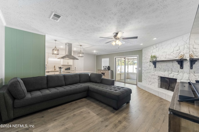 living room featuring crown molding, hardwood / wood-style flooring, ceiling fan, a fireplace, and a textured ceiling