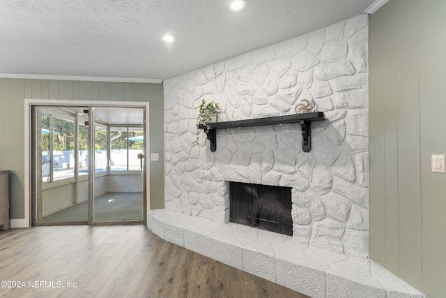 living room with wood-type flooring, ornamental molding, a textured ceiling, and a fireplace