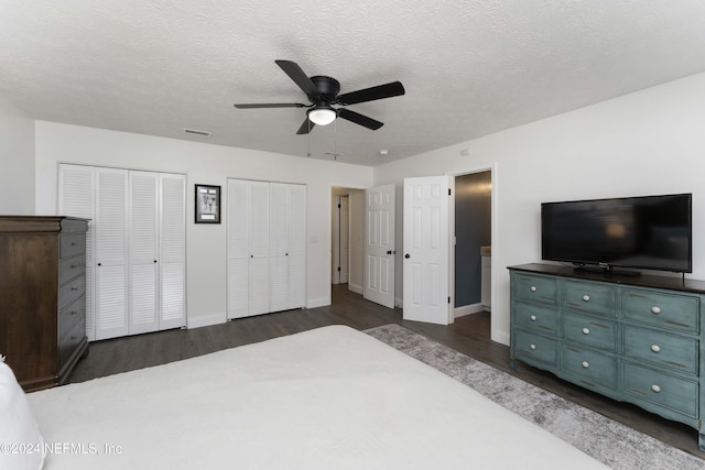 bedroom featuring ceiling fan, a textured ceiling, dark wood-type flooring, and multiple closets