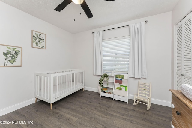 bedroom with a crib, dark wood-type flooring, ceiling fan, and a closet